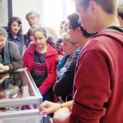 Sybille Merlin, propriétaire de la plupart des objets exposés, commente les vitrines aux collégiens attentifs et étonnés, sous le regard admiratif du principal et d’un professeur.